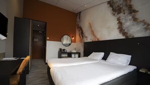 Une chambre d’hôtel avec un grand lit, un bureau, une chaise, un miroir rond et un mur au motif évoquant le marbre.