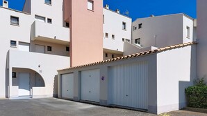 Um edifício com vários andares, área de estacionamento, entrada com portão e placa de proibido estacionar.