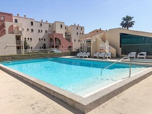 Ein Pool mit Liegestühlen, ein eingezäunter Bereich und ein Gebäude mit Balkonen und einer Palme.