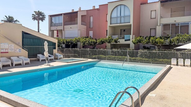 Piscina com espreguiçadeiras e área cercada, rodeada por edifícios com várias andares e varandas.