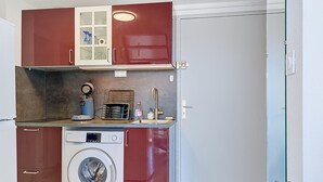 Uma cozinha compacta com máquina de lavar, cafeteira e um pequeno armário com portas de vidro.