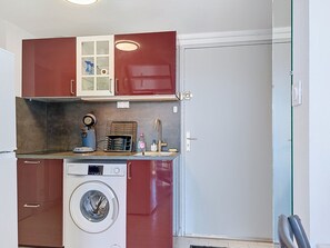 A compact kitchen with a washing machine, a coffee maker, and a small cabinet with glass doors. - Santa Monica 2 by Interhome (Cap d'Agde)