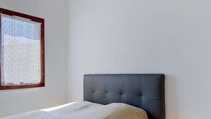 Quarto com cama, janela com cortinas e mesa de cabeceira com abajur.