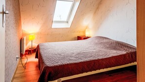 Una camera da letto con soffitto spiovente, un lucernario, un letto con coperta trapuntata, un comodino con lampada e un quadro incorniciato appeso al muro.