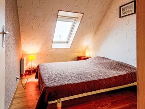 A bedroom with a sloped ceiling, a skylight, a bed with a quilted cover, a bedside table with a lamp, and a framed picture on the wall. - Les Sylvestres by Interhome (Cabourg)