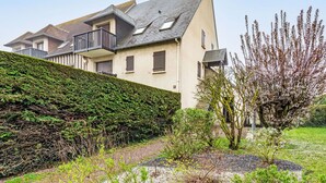 Una casa moderna con tetto spiovente, un balcone e un giardino curato con vialetti in ghiaia e diverse piante.