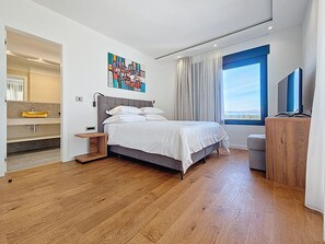 Ein modernes Schlafzimmer mit Bett, ein Badezimmer mit Waschbecken und ein großes Fenster.
