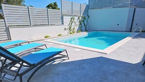 En swimmingpool med ett kaklat poolområde, en metallstege och två blå solstolar.