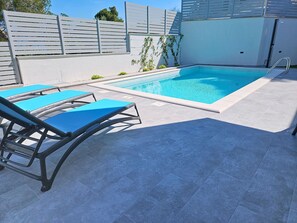 Ein Pool mit Fliesen umgeben, einer Metalltreppe und zwei blauen Liegestühlen.