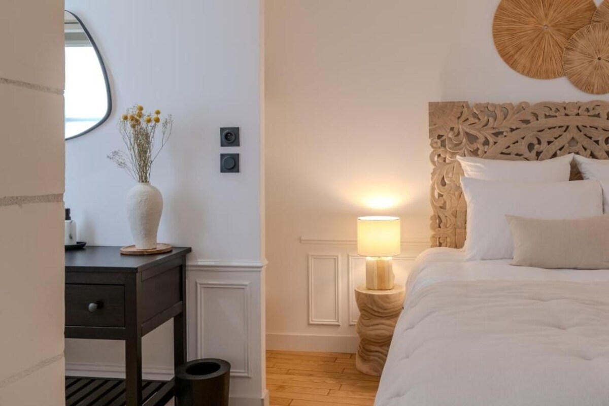 Quarto com cama, mesa de cabeceira, abajur e um objeto decorativo na parede.