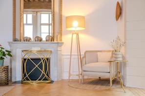 A room with a white sofa, a standing lamp, a gold-framed console table, and a mirror with a gold frame. - La Salamandre (Orléans)