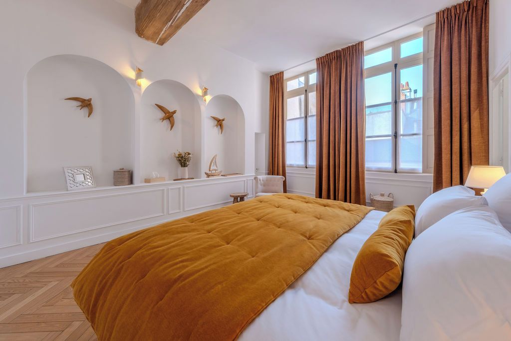 A hotel room with a large bed, a window with curtains, wall-mounted lights, and decorative wall art.