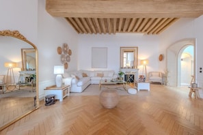 A spacious living room with a herringbone floor pattern, a white sofa set, a fireplace, and a large mirror. - La Salamandre (Orléans)