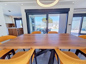 A modern dining area with a wooden table and yellow chairs, large windows, and a view of the outdoors. - Aloa II by Interhome (Brač/Splitska)