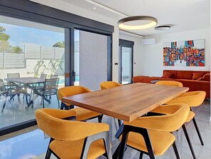 A modern dining area with a wooden table and yellow chairs, a red sofa, and a large window offering a view of the outdoors. - Aloa II by Interhome (Brač/Splitska)