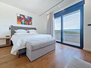Et moderne soveværelse med en stor seng, et natbord, et vindue med udsigt og et farverigt abstrakt billede på væggen.