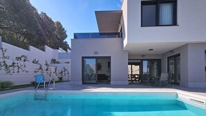 Ett modernt hus med en swimmingpool, en täckt uteplats och utsikt över en sluttning.