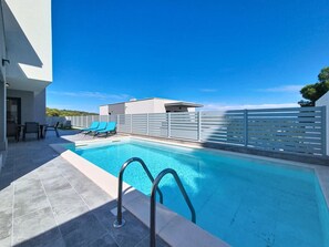 En swimmingpool med moderne design, en hvid bygning og en klar blå himmel.