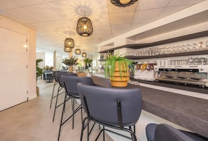 Zona de bar moderna amb tamborets alts, una planta al centre i una màquina de cafè.