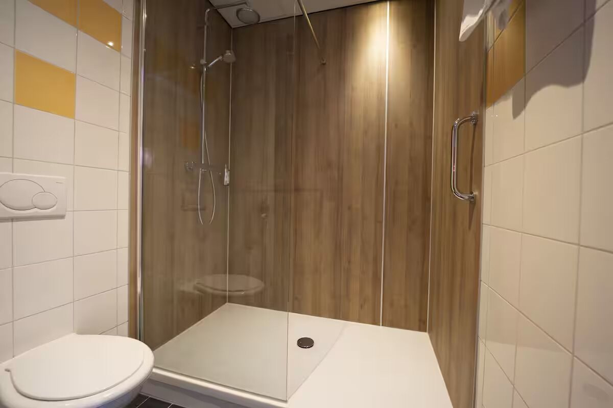 A modern bathroom with a glass-enclosed shower, a white toilet, and a wooden wall panel.