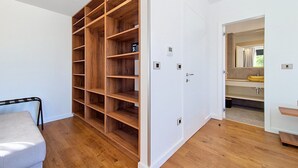 Une pièce avec une étagère en bois, une porte blanche et une salle de bain équipée d’un miroir et d’un lavabo.