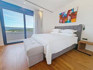 A modern bedroom with a large bed, a bench, a nightstand, a painting, and a view through a large window. - Aloa IV by Interhome (Brač/Splitska)