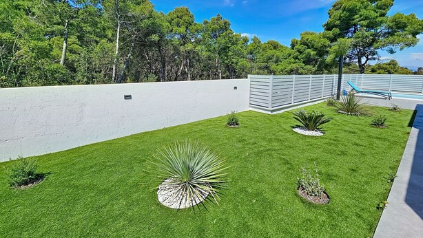 Relvado bem cuidado com uma parede branca e área de piscina.