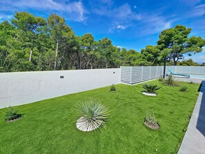 Un césped cuidado con una pared blanca y una zona de piscina.