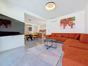 Una sala de estar moderna con un sofá, una mesa de centro y un televisor. Hay una zona de comedor con una mesa y sillas.