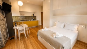 A hotel room with a bed, a dining table with chairs, a kitchen area, and a television mounted on the wall. - Studio apartment | Prime location (Câmara de Lobos)