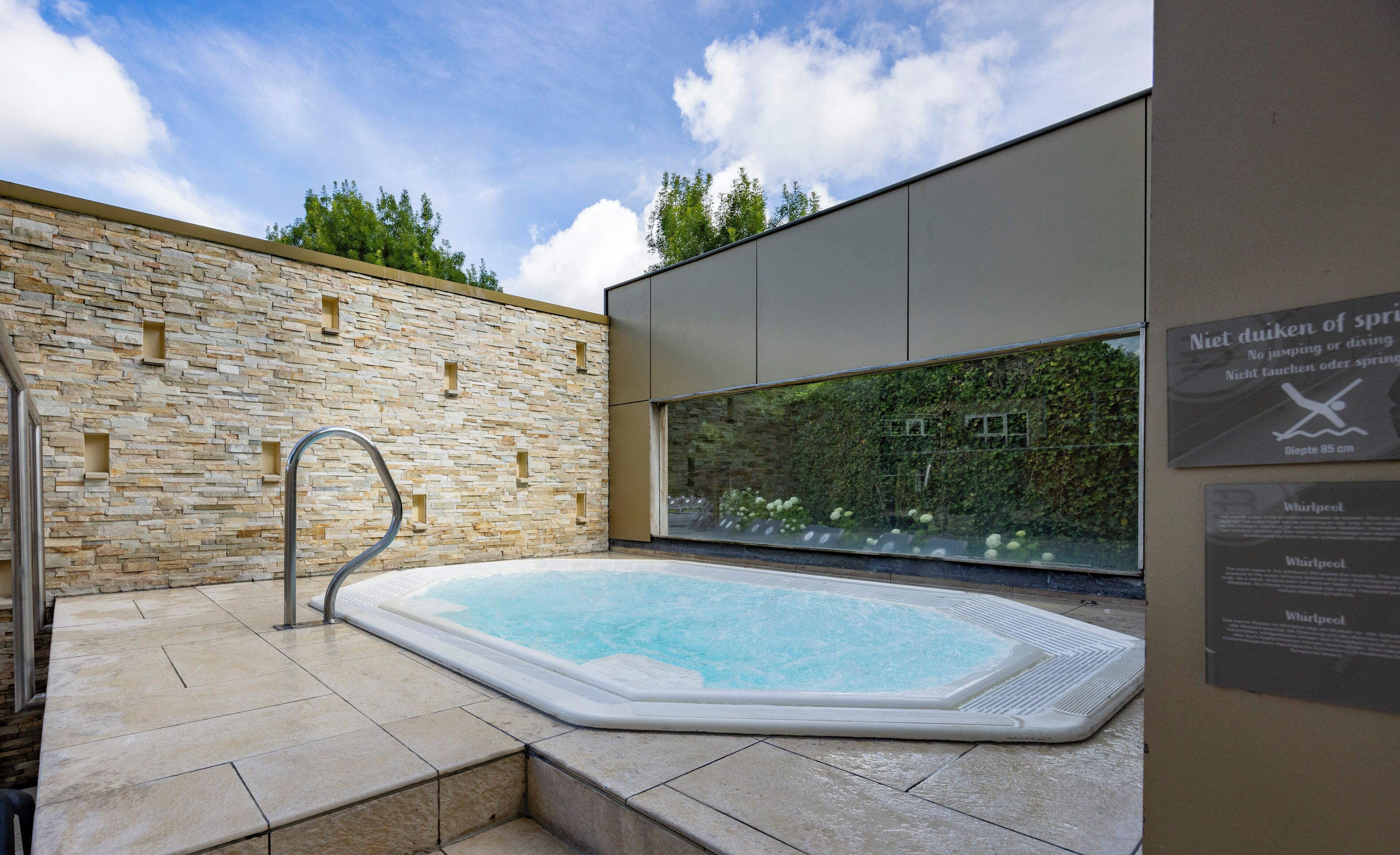 Un espace spa agrémenté d’un mur en pierre, d’un bain à remous et d’une paroi en verre donnant sur un paysage verdoyant.
