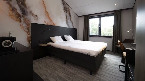 Habitación de hotel moderna con una cama grande, un escritorio, una silla y vistas al exterior a través de la ventana.