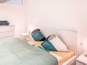Ein ordentlich bezogenes Bett mit einer grünen Decke, zwei Kissen und einem Nachttisch mit einer Lampe.