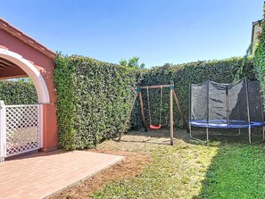A backyard with a swing set, trampoline, and a covered patio area. - Casale Bolgherese by Interhome (Bolgheri)