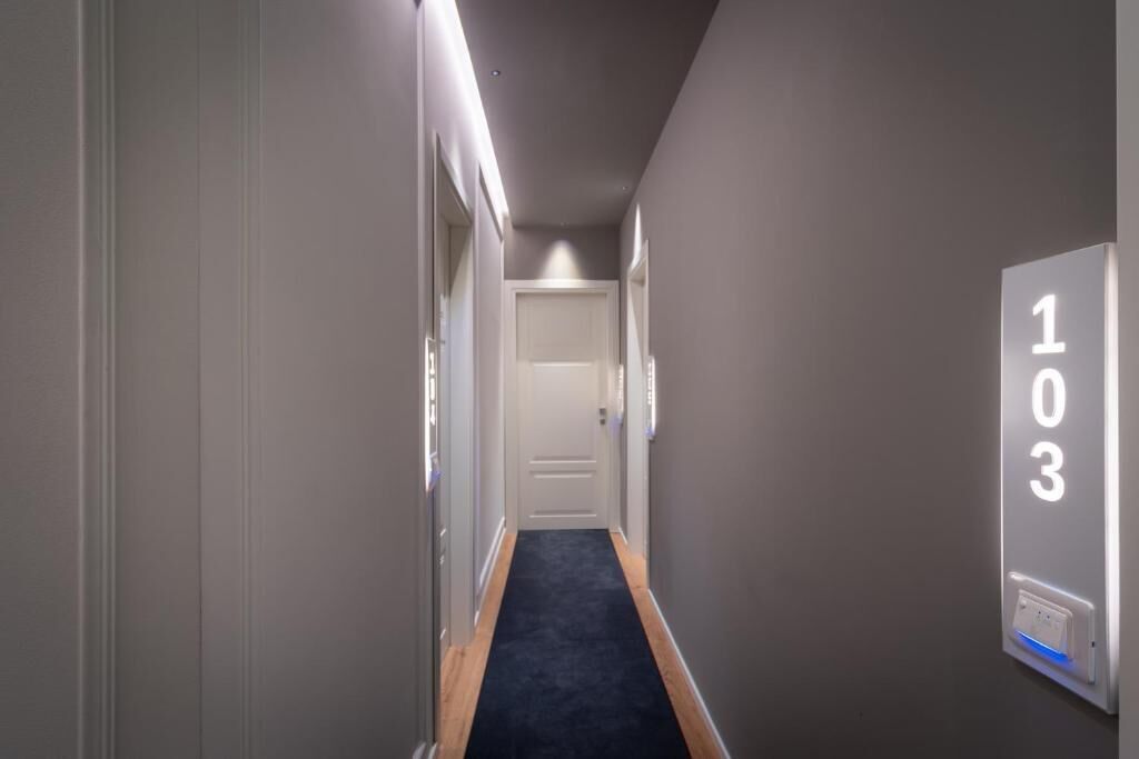 Un pasillo estrecho con alfombra oscura, paredes grises y una puerta al final.