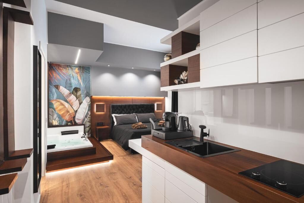 Una cocina moderna con estufa integrada, un comedor con banco y un dormitorio con cama grande y un cuadro.