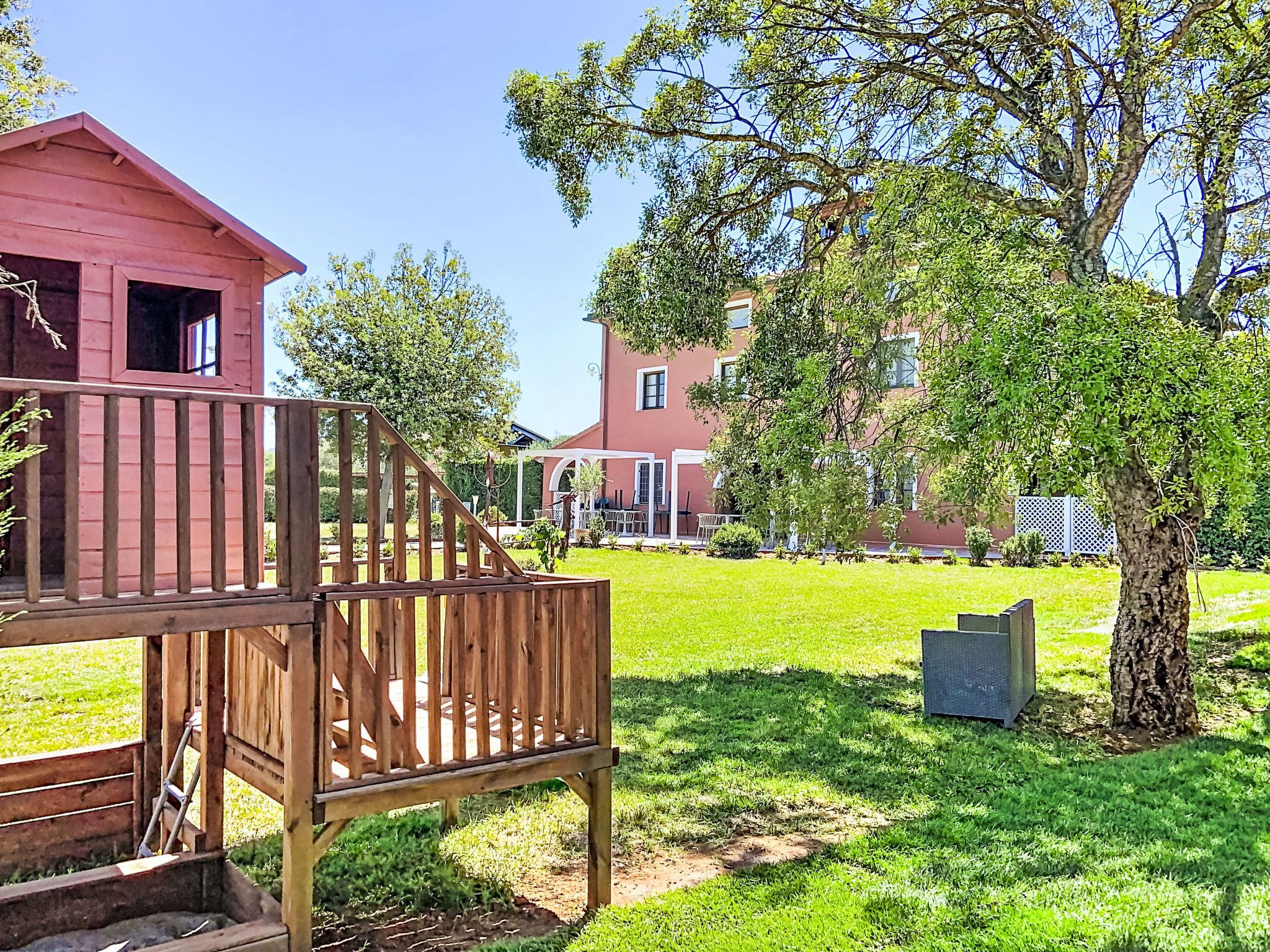 A red building with a wooden deck and a tree in the yard.