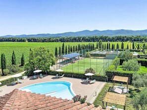 Une piscine, des chaises longues et un court de tennis, le tout entouré de verdure et de montagnes.