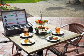 A table with a tiered dessert stand, plates with sandwiches and cupcakes, and glasses of a beverage.