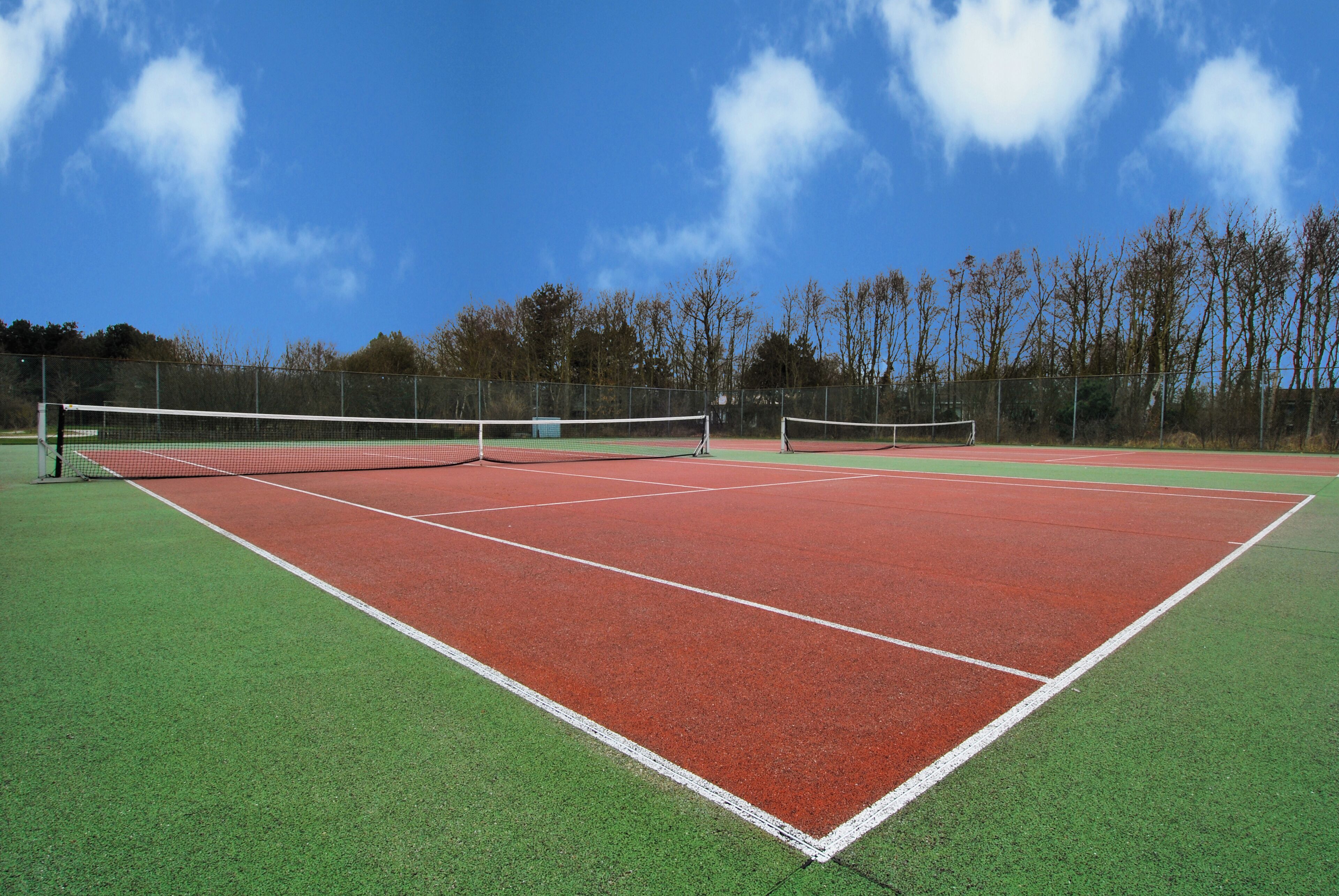 Ein Tennisplatz mit Netz, umgeben von einer grünen Wiese und Bäumen.