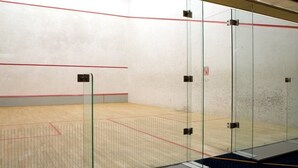Un court de squash avec des murs en verre, un plancher en bois et une ligne rouge délimitant la zone de jeu.