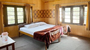 A wooden room with a bed, two windows, and a table with a water bottle. - Lakshmi Guest House (Srinagar)