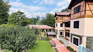 A two-story building with a garden in front, a paved walkway, and a tree. - Lakshmi Guest House (Srinagar)