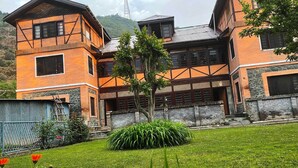 A two-story building with a stone foundation and wooden upper structure, surrounded by a well-maintained lawn with orange flowers. - Lakshmi Guest House (Srinagar)