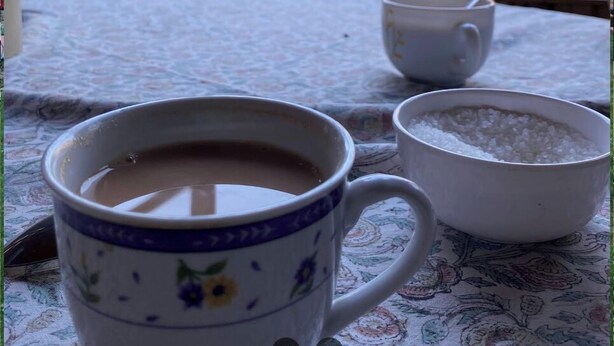 A table with a floral tablecloth, a cup of coffee, and a bowl of sugar. - Lakshmi Guest House (Srinagar)