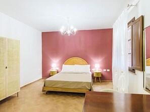 Ein Schlafzimmer mit einem Bett, zwei Nachttischlampen, einer Pendelleuchte, einem Kleiderschrank und einem Fenster mit Vorhängen.