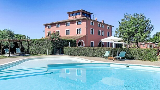 A swimming pool with lounge chairs and a building with a red facade in the background. - Casale Bolgherese by Interhome (Bolgheri)
