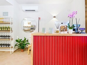 A reception desk with a red panel, a mirror, a wall-mounted air conditioner, and shelves with bottles. - Casale Bolgherese by Interhome (Bolgheri)