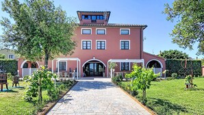 A two-story building with a paved pathway leading to the entrance, surrounded by greenery and a clear sky. - Casale Bolgherese by Interhome (Bolgheri)