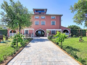 A two-story building with a paved pathway leading to the entrance, surrounded by greenery and a clear sky. - Casale Bolgherese by Interhome (Bolgheri)